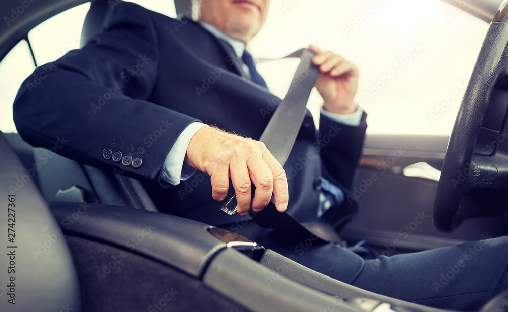 transport, business trip, safety and people concept - senior businessman fastening seat belt before driving car
