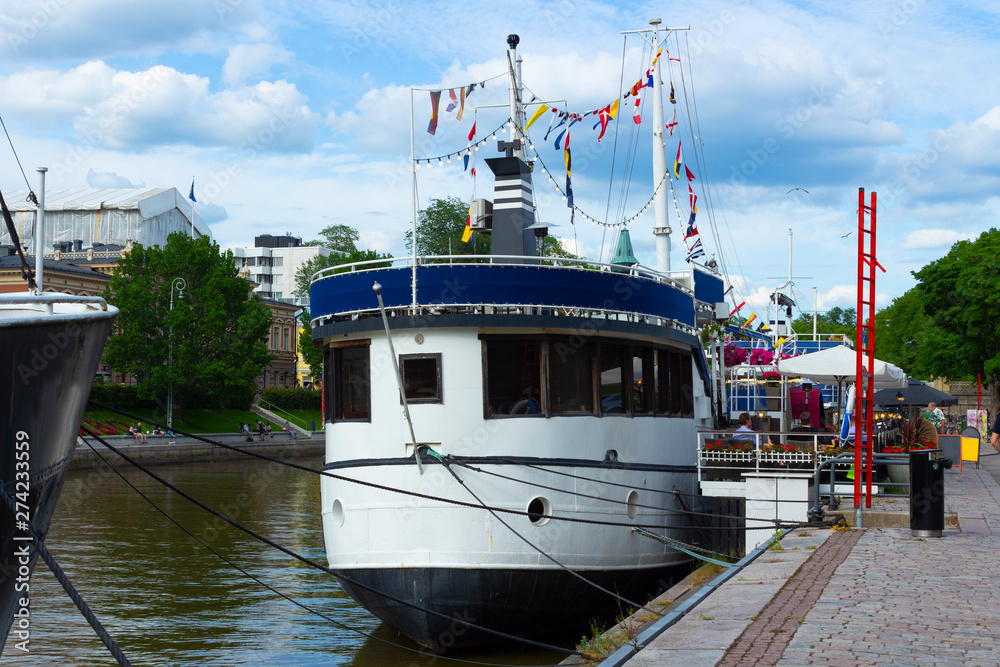 Naklejka premium An old vintage ship laid up at the pier of the embankment of the Auraioki River in the city of Turko Abo in Finland.