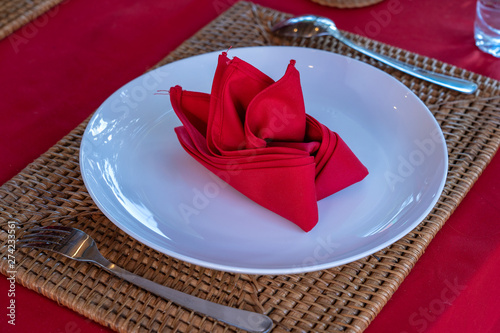 Elegant table setting with fork, spoon, white plate and red napkin in restaurant . Nice dining table set with arranged silverware and napkins