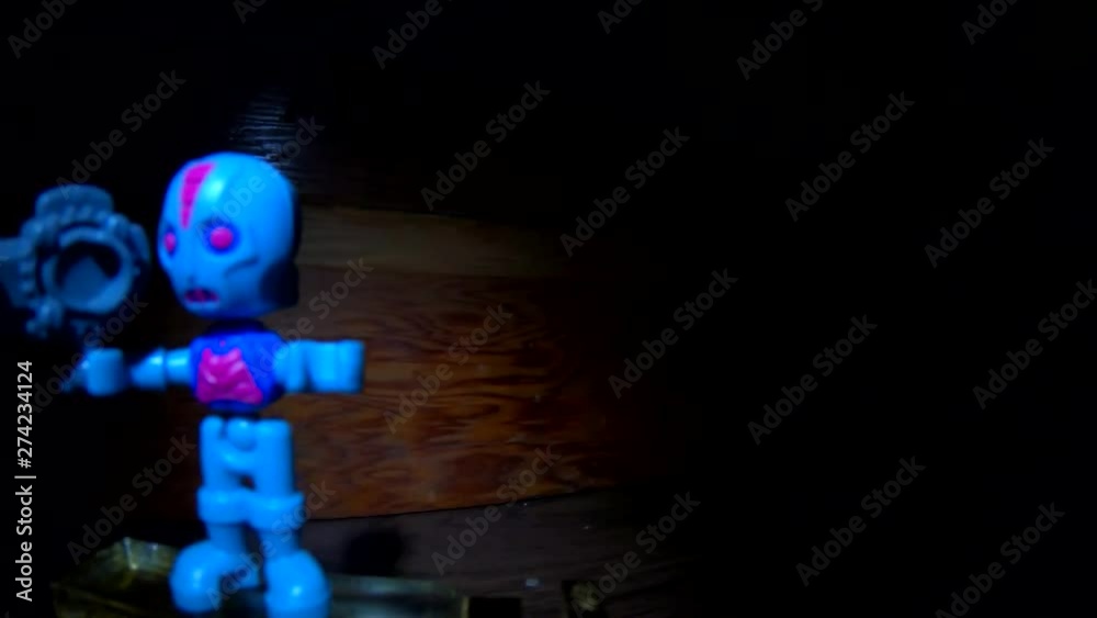 Blue alien toy figure standing on a platform in a spot light on a wooden table. ( 4k footage ) Blue alien toy figure standing on a platform in a spot light on a wooden table. ( 4k footage )
