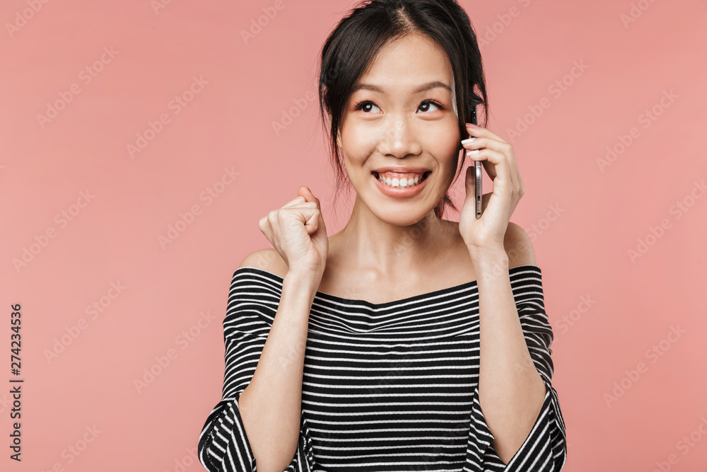 Image of happy asian woman dressed in basic wear smiling while talking on mobile phone Image of happy asian woman dressed in basic wear smiling while talking on mobile phone