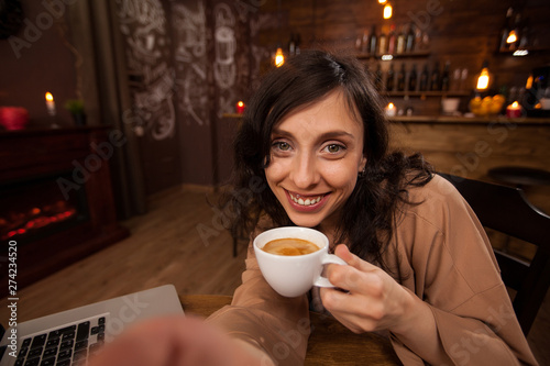 Attractive young woman holding a camera and a cup of coffee taking a selfie
