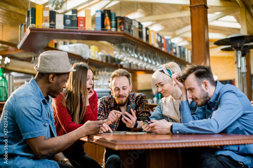 Young college students or coworkers using smartphones together at coffee shop, diverse group. Casual business, freelance work at cafe, social meeting, or education concept