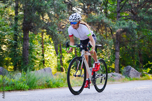 Young Woman Cyclist Riding Road Bicycle on the Free Road in the Forest at Hot Summer Day. Healthy Lifestyle Concept.