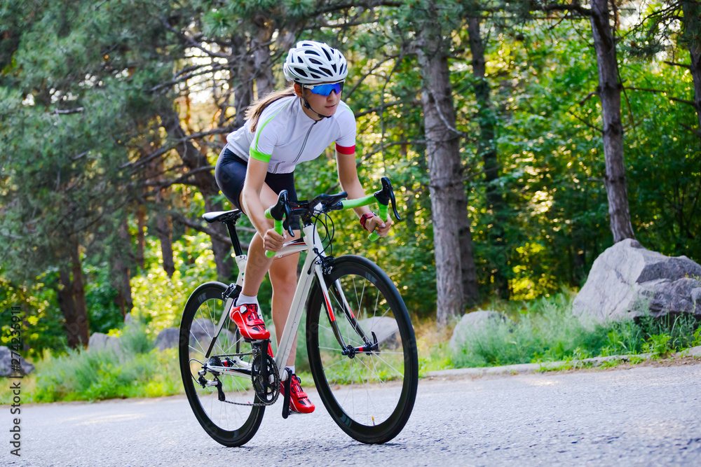 Young Woman Cyclist Riding Road Bicycle on the Free Road in the Forest at Hot Summer Day. Healthy Lifestyle Concept.