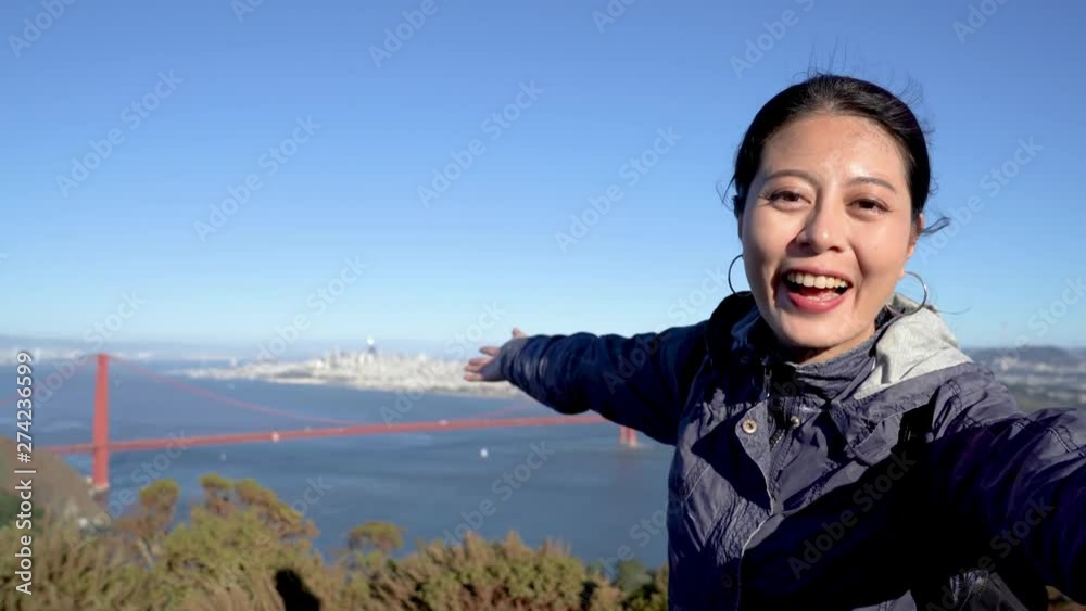 Happy asian girl traveler making selfie or video phone call with golden gate bridge in background surrounding by blue ocean sea and sky. female smiling talking laughing waving hands into camera. Happy asian girl traveler making selfie or video phone call with golden gate bridge in background surrounding by blue ocean sea and sky. female smiling talking laughing waving hands into camera.