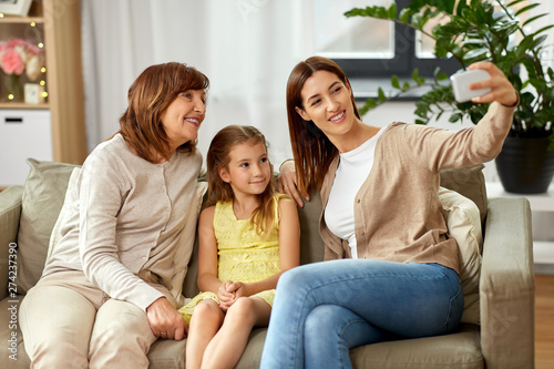 family, generation and technology concept - happy mother, daughter and grandmother taking selfie by smartphone at home