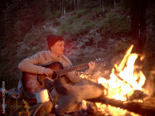 Camping at night around a campfire in nature to the sound of a guitar.