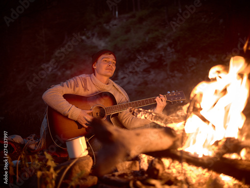 Camping at night around a campfire in nature to the sound of a guitar.