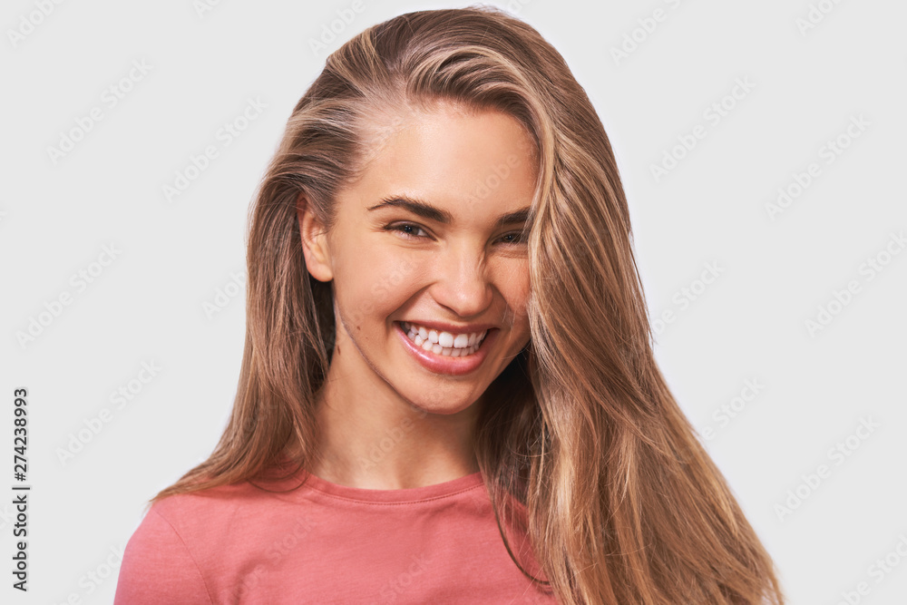 Portrait of blonde good-looking young woman, with beautiful healthy hair, smiles positively wearing casual outfit and looking to the camera, isolated on white studio wall. People emotions Portrait of blonde good-looking young woman, with beautiful healthy hair, smiles positively wearing casual outfit and looking to the camera, isolated on white studio wall. People emotions