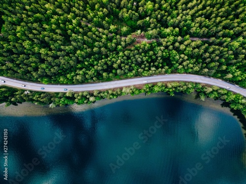 Aerial view of road between green forest and blue lake in Finland