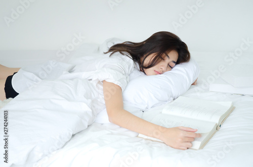 Women are reading books And she is having sleepiness And slept beside her book On the bed in the room.o not focus on the main object of this image.Copy space.