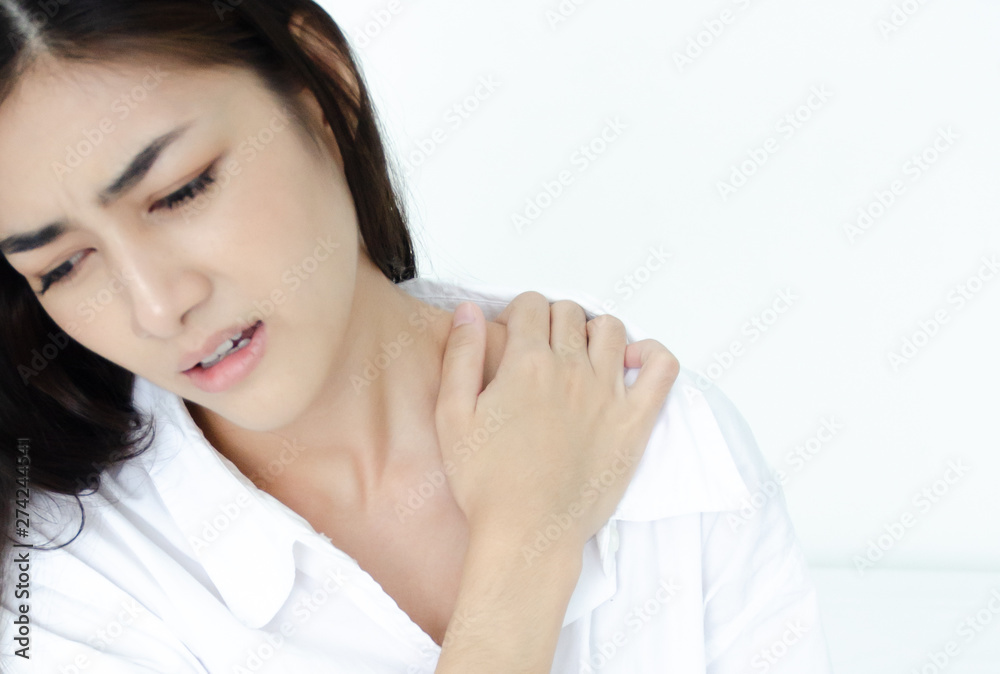 Asian women wear white pajamas in the bedroom. She has pain in the neck area.Do not focus on the main object of this image. Asian women wear white pajamas in the bedroom. She has pain in the neck area.Do not focus on the main object of this image.