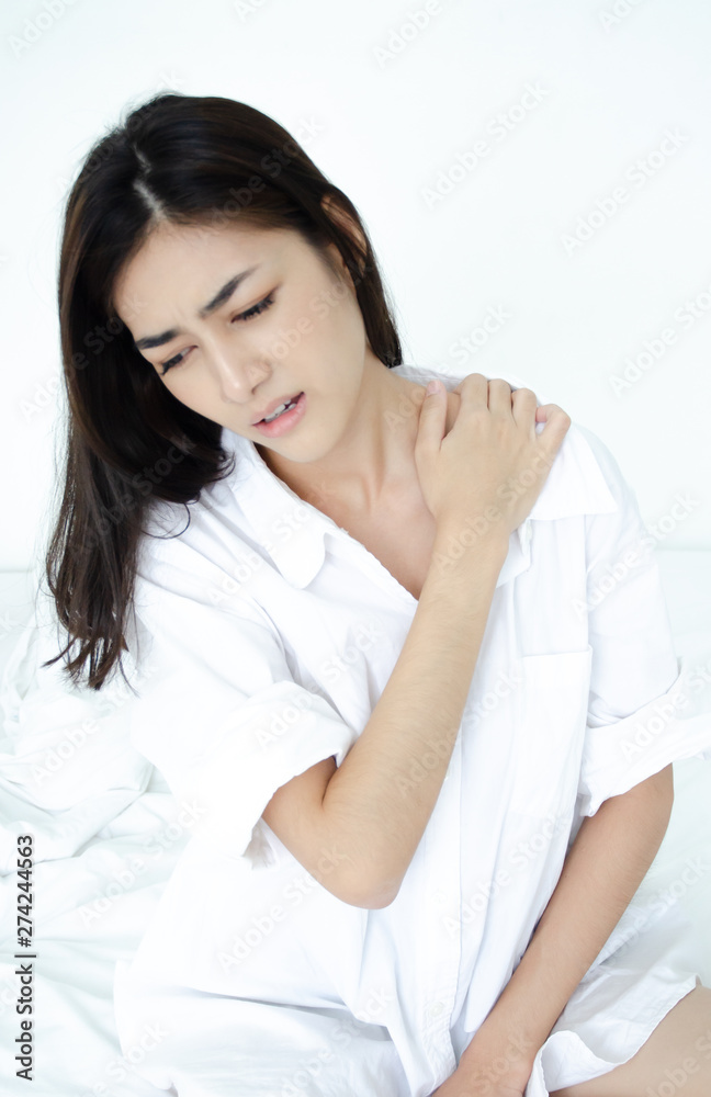 Asian women wear white pajamas in the bedroom. She has pain in the neck area. Asian women wear white pajamas in the bedroom. She has pain in the neck area.