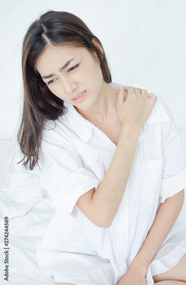 Asian women wear white pajamas in the bedroom. She has pain in the neck area. Asian women wear white pajamas in the bedroom. She has pain in the neck area.