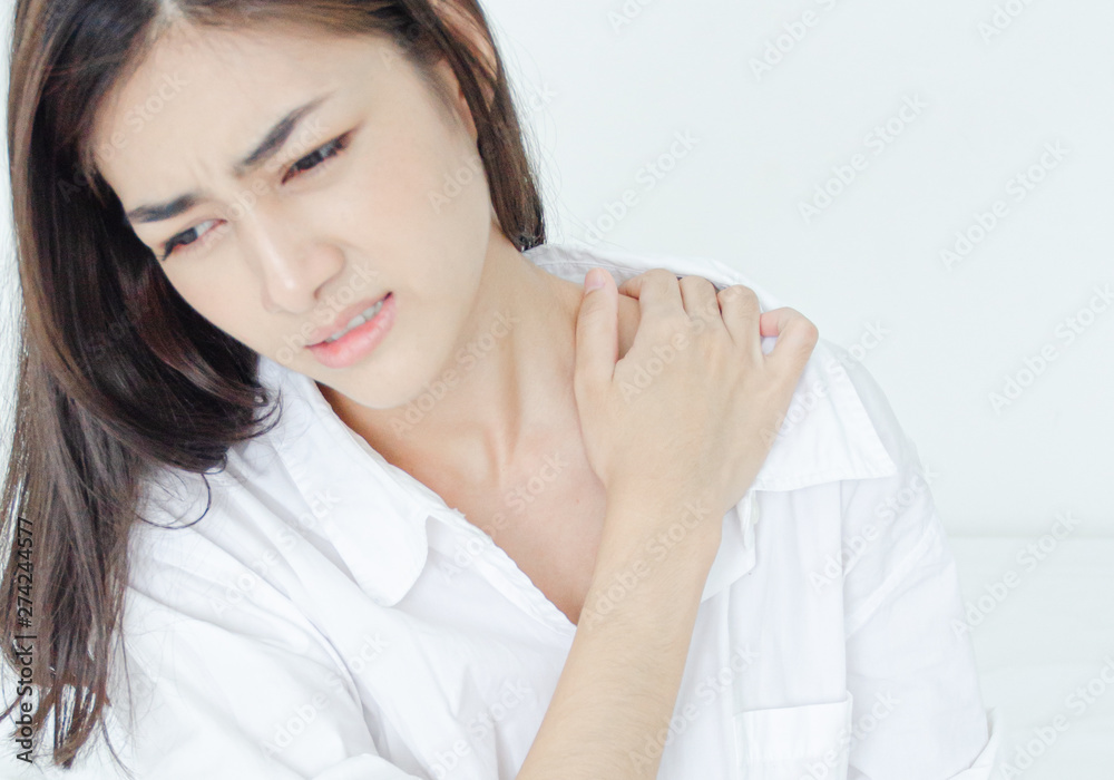 Asian women wear white pajamas in the bedroom. She has pain in the neck area.Do not focus on the main object of this image. Asian women wear white pajamas in the bedroom. She has pain in the neck area.Do not focus on the main object of this image.