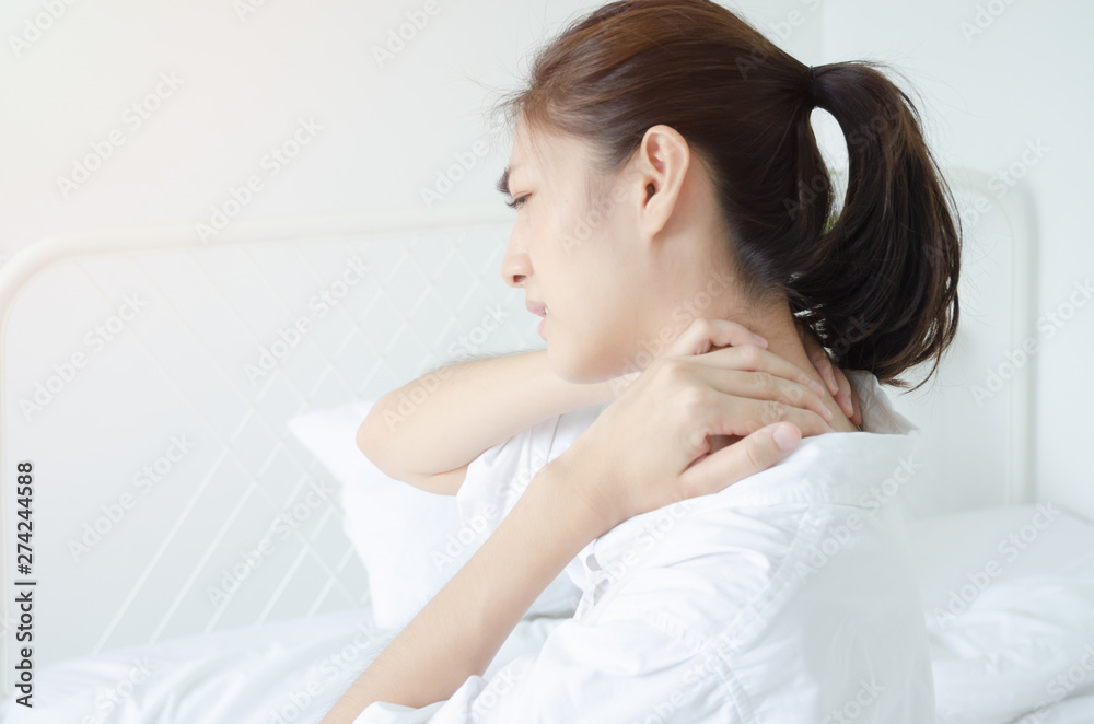 Asian women wear white pajamas in the bedroom. She has pain in the neck area.Do not focus on the main object of this image. Asian women wear white pajamas in the bedroom. She has pain in the neck area.Do not focus on the main object of this image.