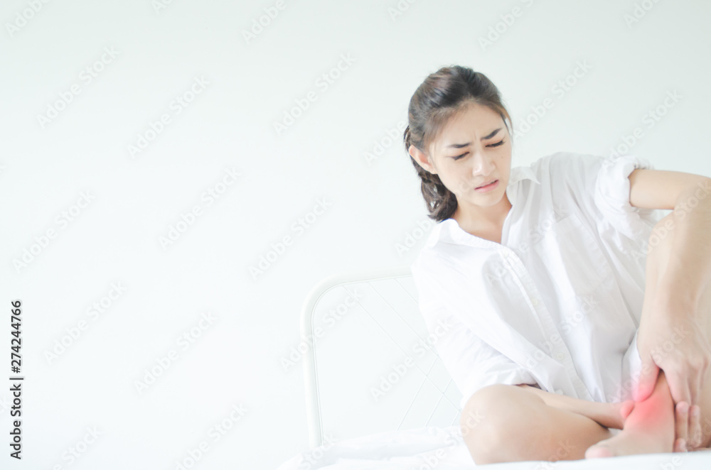Asian girl wearing white dress have leg pain. The woman was squeezing her leg in a white bedroom with sunshine.Warm tone.Do not focus on objects. Asian girl wearing white dress have leg pain. The woman was squeezing her leg in a white bedroom with sunshine.Warm tone.Do not focus on objects.