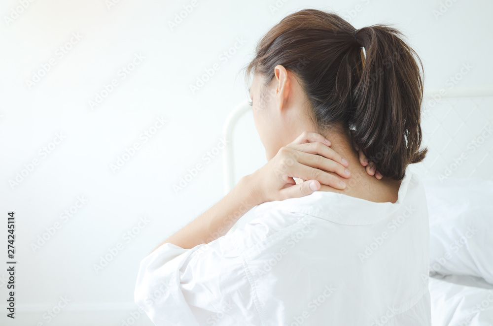 Asian women wear white pajamas in the bedroom. She has pain in the neck area.Do not focus on the main object of this image. Asian women wear white pajamas in the bedroom. She has pain in the neck area.Do not focus on the main object of this image.