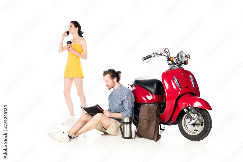 full length view of girl talking on samrtphone, holding paper cup and young man looking at map, sitting near red scooter isolated on white
