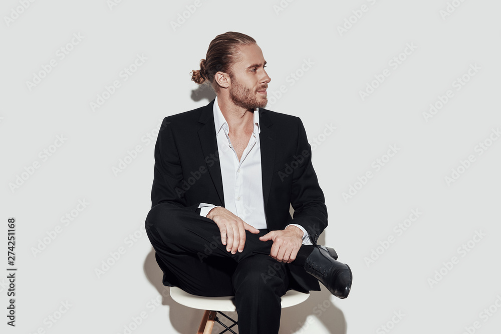 Time to make decision. Handsome young man in full suit looking away while sitting against grey background Time to make decision. Handsome young man in full suit looking away while sitting against grey background