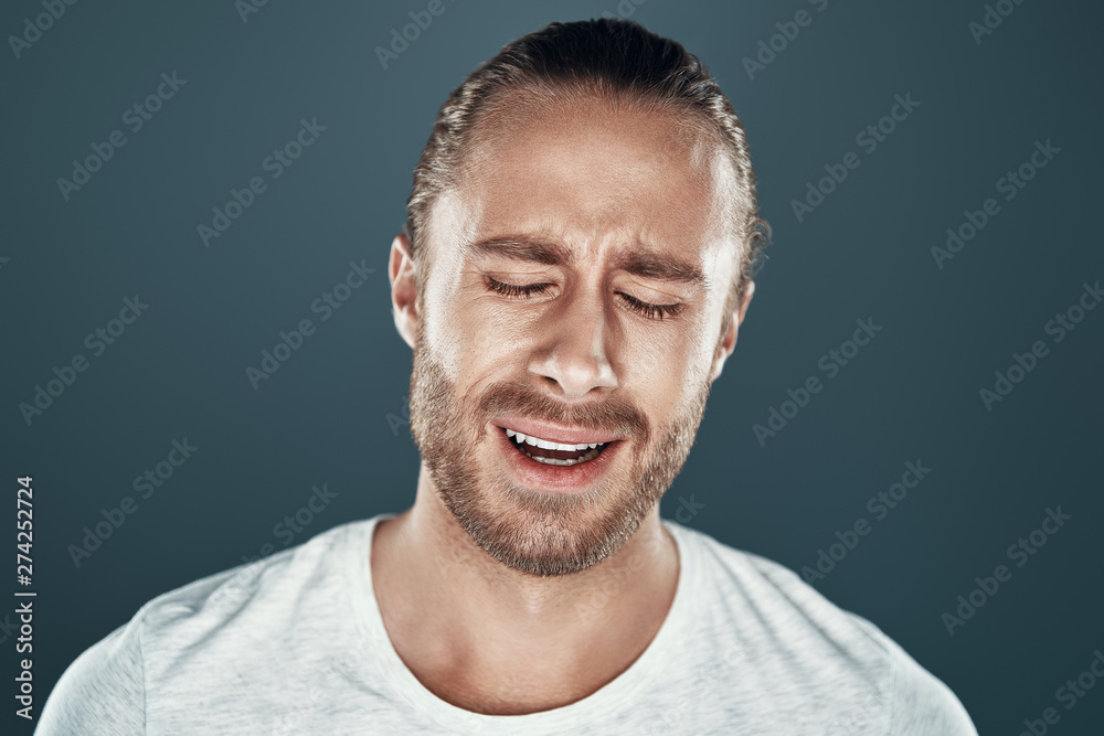 Hysteria. Frustrated young man making a face while standing against grey background