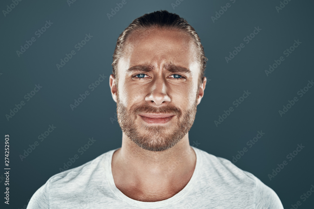 Fototapeta premium Feeling displeased. Handsome young man looking at camera while standing against grey background