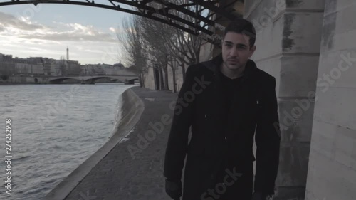 Handsome young depressed man walking on the banks of the Seine in Paris winter in the middle of the afternoon, thinking sadly to his ex girlfriend. Medium Shot.