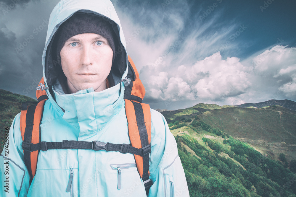 Young male hiker on cloudy landscape background looking at camera. Front view. Active lifestyle and tourism concept.