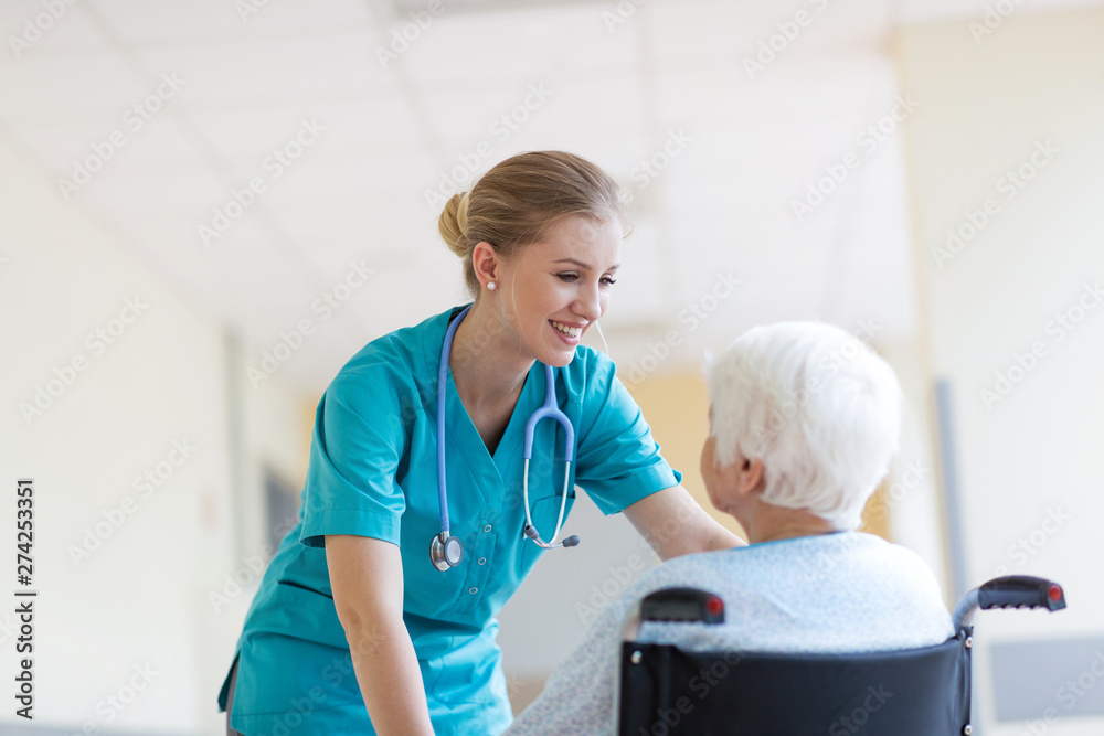 Senior woman in wheelchair with nurse in hospital - obrazy, fototapety, plakaty 