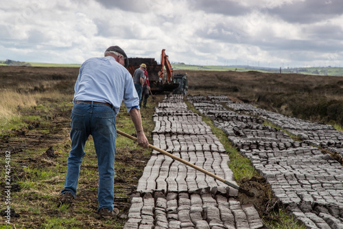 Men cutting turf in a peat bog field in rural Ireland, Peat bog is cultivated as a fuel source during spring season in the republic of Ireland  photo