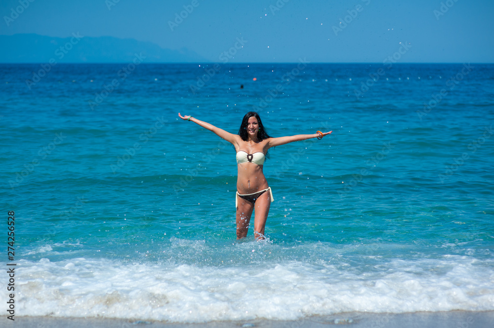 girl in bikini playing with water on the beach of maldives. Young slim model with tanned skin having fun in the ocean.
