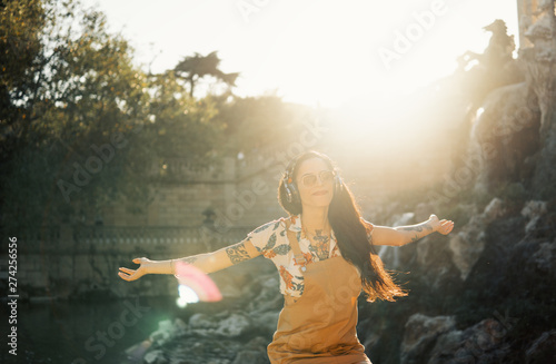 transgender model wearing sunglasses in the green park. She is listening to music with headphones and enjoys