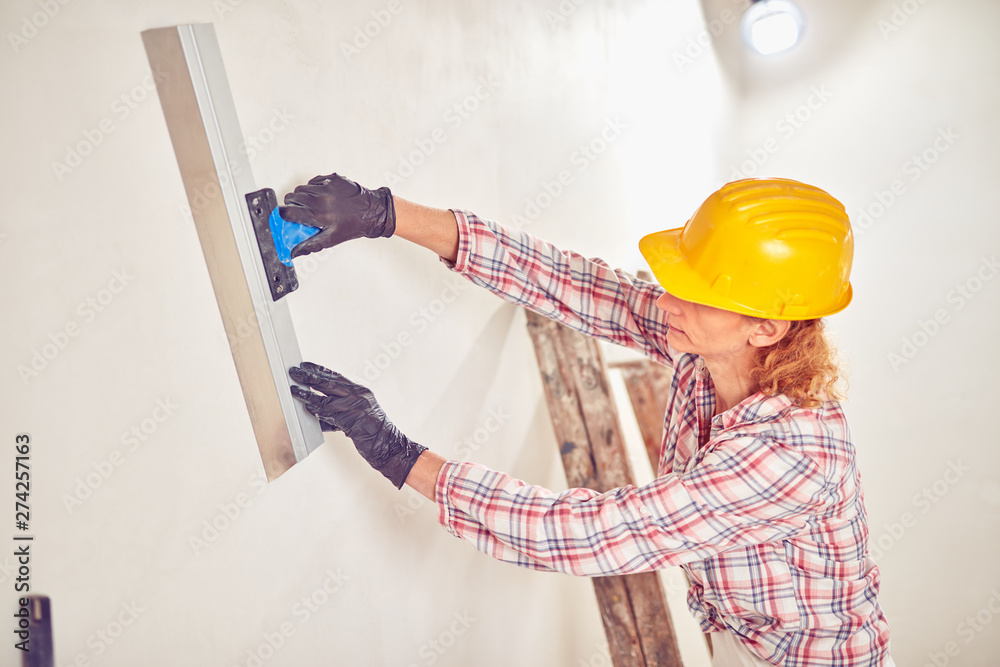 Working woman plastering / painting walls inside the house. - obrazy, fototapety, plakaty 