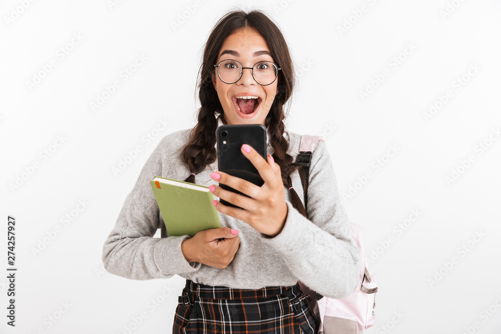 Photo closeup of excited teenage girl wearing eyeglasses laughing while holding studying books and smartphone Photo closeup of excited teenage girl wearing eyeglasses laughing while holding studying books and smartphone