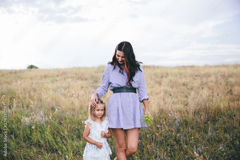 Mother and daughter are walking in wheat field at spring time.