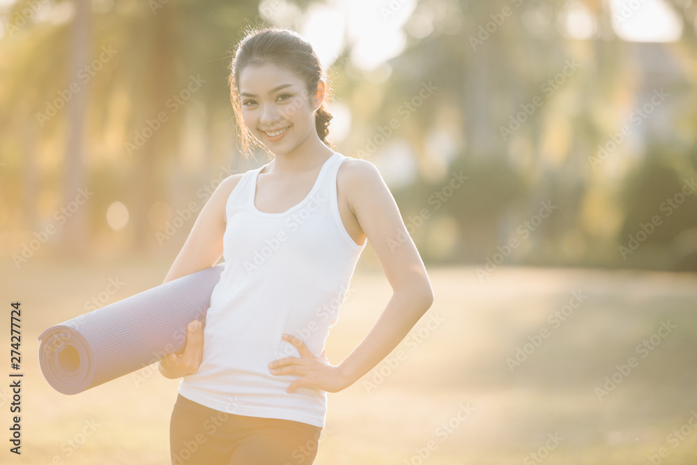 Fototapeta premium woman carrying a yoga mat outdoors and smiling