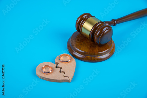 Wedding rings on the figure of a broken heart from a tree, hammer of a judge on a blue background. Divorce divorce proceedings
