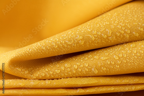 Close-up waterproof and water repellent fabric.  Water drops on textile. Folded canvas of yellow fabric