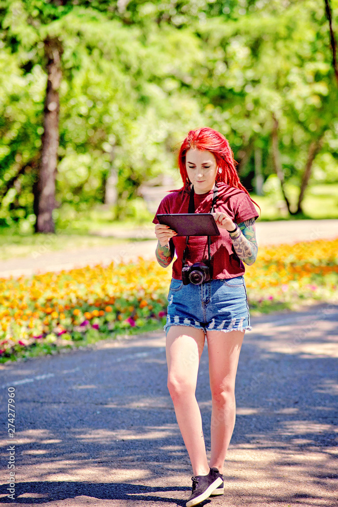 Young girl with red hair and dreadlocks walks in a summer park