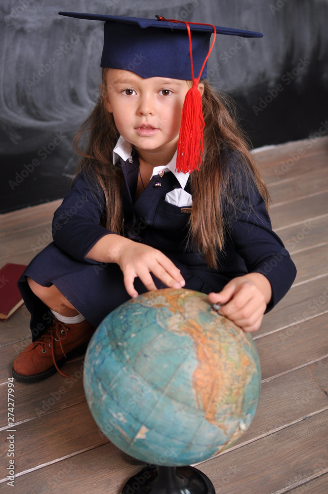 Fototapeta premium Portrait of happy school girl in graduation hat.Go to school for the first time.Young first-grade girl exploring the globe.school and education concept