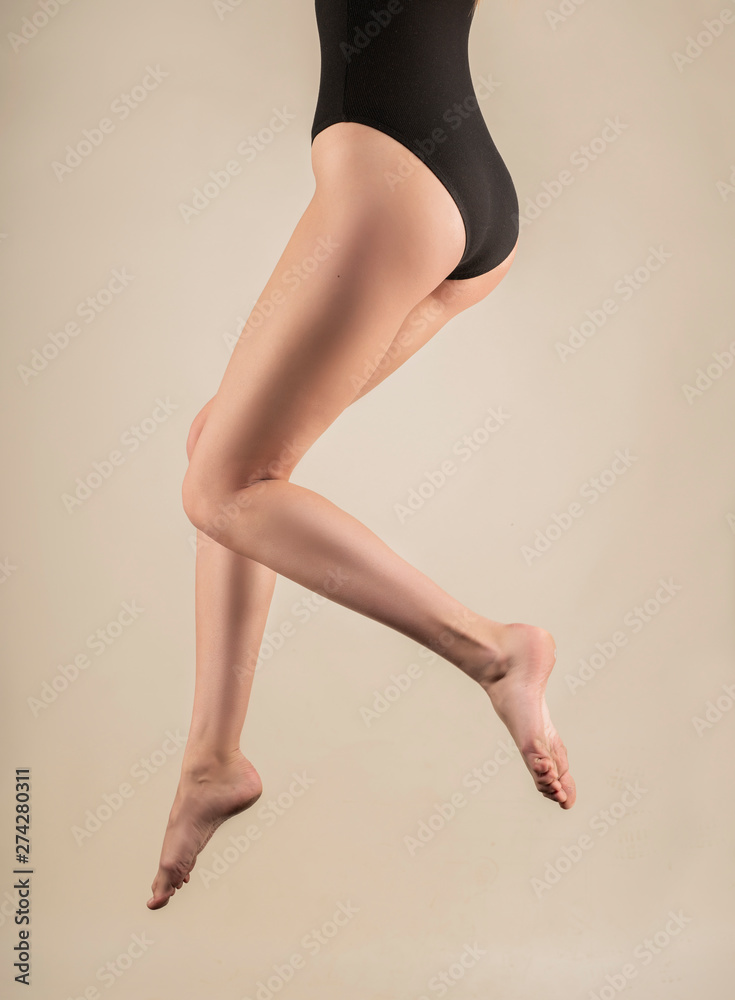 Long beautiful slender female legs hanging in the air in the jump. The girl is dressed in a black body. Isolated on a light background. Fashionable, advertising and commercial design. Long beautiful slender female legs hanging in the air in the jump. The girl is dressed in a black body. Isolated on a light background. Fashionable, advertising and commercial design.