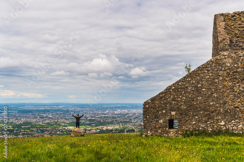 Photography Happy male tourist with hands in the air, enjoying the breathtaking view from the top of Montpelier Hill over Dublin City and bay in Ireland, with the ruins of the famous HellFire Club behind