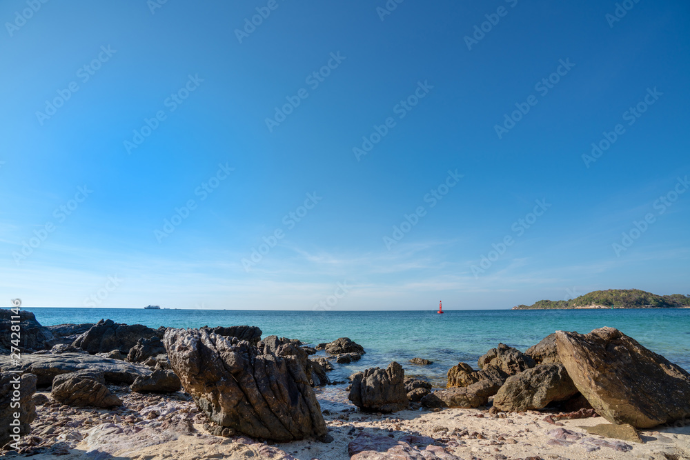 Landscape wide shot elective focus of rocky sand beach at tropical island in summer. Red buoy floating in blue sea with sky and clouds backgrounds. The sun glimmering sunlight peeking the sea surface
