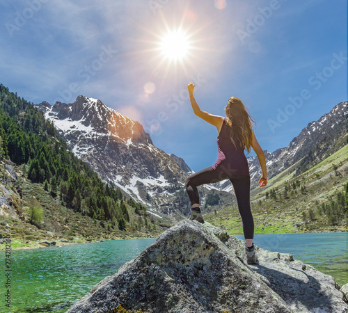 Frau in Siegerpose auf einem Felsen an einem Bergsee