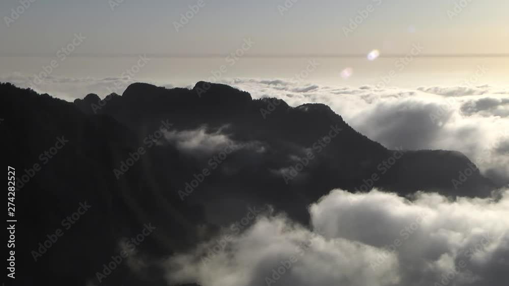LOCKED OFF TIMELAPSE of rolling clouds moving around silhouette of mountains
