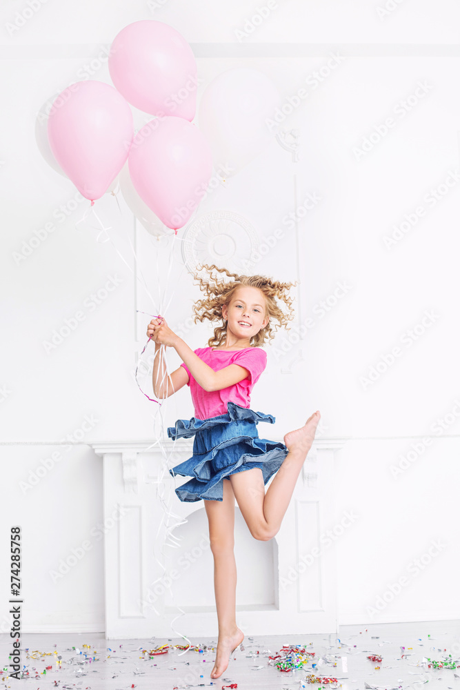 Happy beautiful cute child girl with smile at holiday party with balloons and confetti in white room