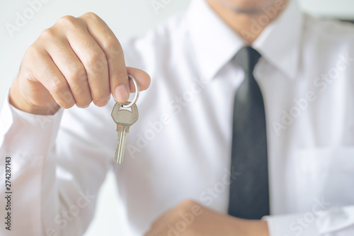 Young Asian man receiving new apartment or room key from realtor or real estate sales agent after finish a rental or buying contract.