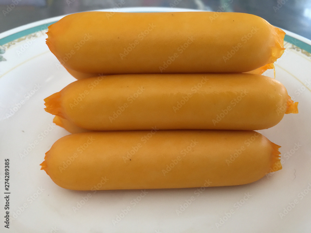 Close-up of a yellow-orange cheese sausage on a white plate. Close-up of a yellow-orange cheese sausage on a white plate.