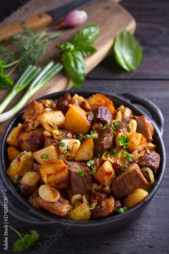 Fried beef and  potatoes with onions and garlic served in black dish on wooden background